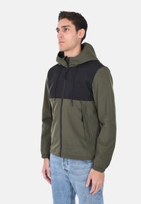 Giacca con cappuccio verde oliva con pannello superiore nero. Caratterizzata da chiusura con zip, polsini elasticizzati e tasche laterali. Texture liscia e leggera.