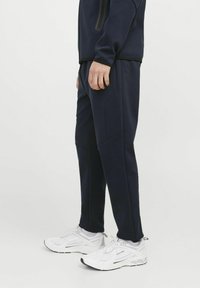Jogging en bleu marine en tissu doux, avec des poches latérales et une coupe fuselée, associés à des baskets en mesh blanches.