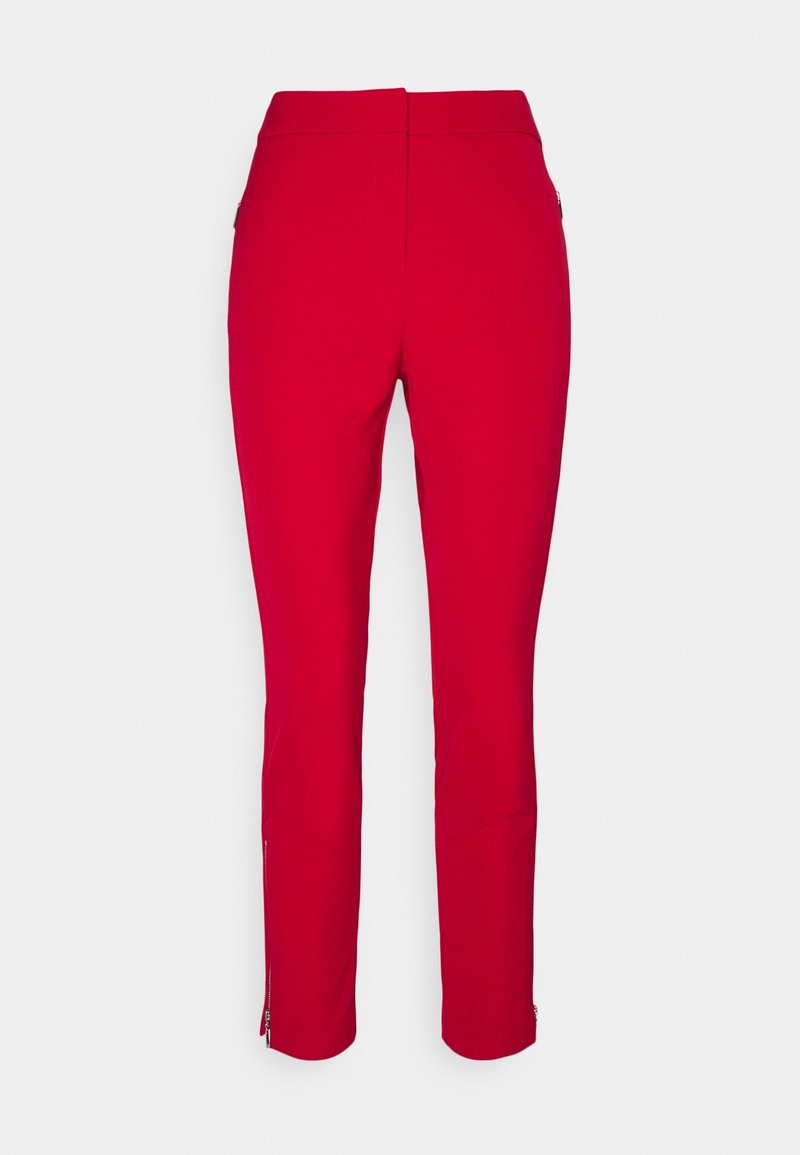 Pantalon rouge slim avec fermetures éclair sur le côté et à la cheville, vu de dos sur un fond clair uni.