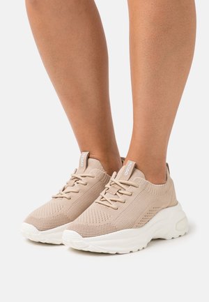 Beżowe dzianinowe sneakersy z teksturowaną cholewką, białą podeszwą i sznurówką. Oferują miękką kołnierz i metkę z logo na języku.