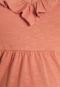 Bluzka w kolorze brzoskwiniowym z teksturowanej tkaniny, z falbaniastym dekoltem i zgromadzoną linią dołu. Miękki, lekki materiał.