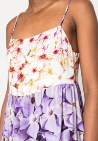 Robe florale avec un corsage ajusté ornée de fleurs roses et blanches ; jupe violette évasée avec de grands motifs floraux ; fines bretelles ; tissu léger.