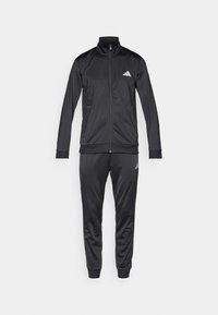 Black tracksuit made of smooth, lightweight fabric. Zip-up jacket with high collar and white logo. Matching pants with cuffed ankles.