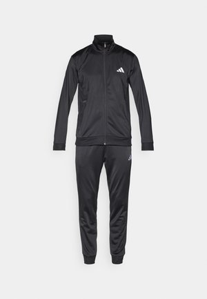 Black tracksuit made of smooth, lightweight fabric. Zip-up jacket with high collar and white logo. Matching pants with cuffed ankles.