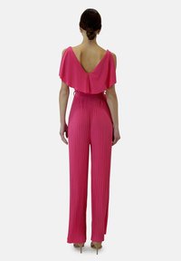 Mono rosa con pliegues, mangas al descubierto, escote en V profundo en la espalda y cintura ajustada. Tejido suave con un diseño fluido, combinado con tacones.