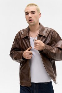 Bružas ādas pieguloša jaka ar lielu apkakli, brīvs fit un izteikta šuvju rakstura. Valkāta virs baltas t-krekla un zilajiem džinsiem.