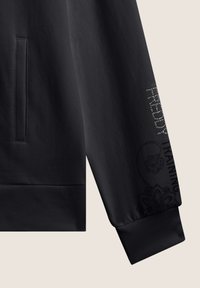 Felpa nera con una texture liscia, caratterizzata da una tasca laterale, polsini a costine e elementi di design stampati. Testo scintillante "FREDDY TRAINING".