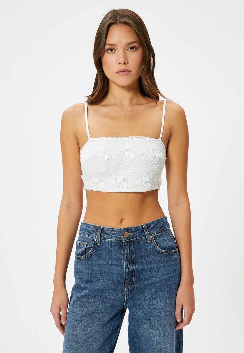 Witte cropped top van textuurstof, met bloemembroidery en dunne bandjes, gecombineerd met hoge blauwe denim jeans.