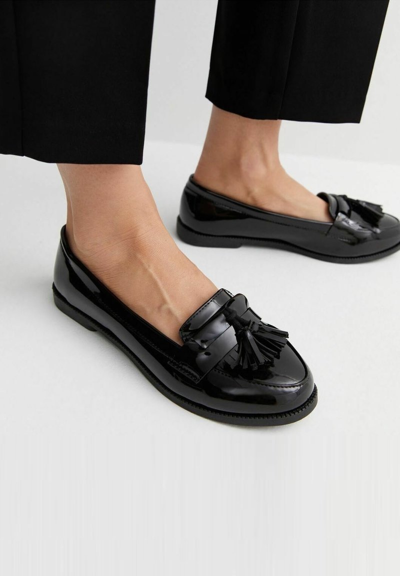 Mocassins en cuir verni noir avec un détail pompon, bout arrondi, et design élégant. Semelle en caoutchouc offrant une bonne adhérence, adaptés pour un usage décontracté.