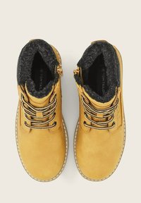 Gelbe Wildleder-Stiefeletten mit schwarzem Kunstfellfutter und dicken schwarz-weißen Schnürsenkeln. Verfügt über einen seitlichen Reißverschluss und weiße Nähdetails.