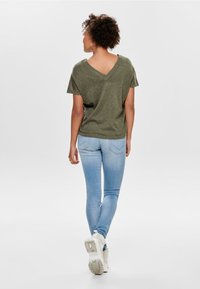 Camiseta verde oliva de cuello en V y mangas cortas, combinada con jeans ajustados de color azul claro y zapatillas blancas. Textura suave con un ajuste relajado.