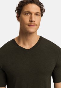 Tmavě zelené tričko s krátkým rukávem a výstřihem do V, vyrobené z měkkého materiálu s texturovaným povrchem. Jednoduchý design bez výrazných vzorů nebo akcentů.