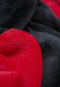 Manta de felpa roja y negra, con una textura suave y aterciopelada que presenta una sección roja intensa y vibrante en contraste con un área negra más oscura.