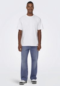 Bílé bavlněné tričko s krátkými rukávy, doplněné světlými modrými džíny s rovnými nohavicemi a černobílými teniskami.