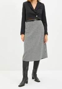 Blazer negro corto con un solo botón, combinado con una falda de pata de gallo en blanco y negro hasta la rodilla y botas de tacón negro hasta la rodilla.