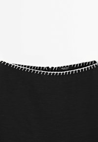 Vêtement noir à texture lisse, présentant un col rond avec des surpiqûres blanches contrastantes et une fermeture éclair au dos.