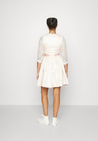 Robe rose clair avec un corsage ajusté, des manches en dentelle trois-quarts et une jupe évasée. Détail en ruban à la taille et bottines blanches à la cheville.