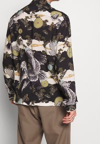 Koszula z długim rękawem z kolorowymi wzorami ptaków i kwiatów na czarnym tle. Wykonana z lekkiego materiału, z kołnierzykiem typu spread i mankietami na guziki.
