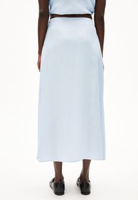 Lichtblauwe, lange rok met een zachte textuur en zijsplitten, gecombineerd met zwarte schoenen, gezien vanaf de achterkant.