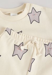 Ensemble en coton crème clair comprenant un pull avec des motifs d'étoiles grises et un pantalon assorti à taille élastique avec cordon de serrage.