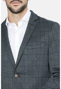Blazer azul marino y gris a cuadros con un solo botón marrón. Presenta un cuello en pico y una tela texturizada, combinado con una camisa de vestir blanca.