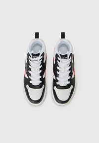 Divas baltas, melnas un sarkanas Reebok sporta apavi ar baltajām auklām, skatīti no augšas uz vienkārša balta fona.