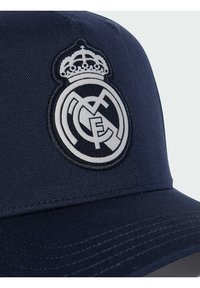Casquette bleu marine en tissu, ornée d'un logo Real Madrid en blanc brodé et d'une couronne à l'avant. Visière structurée avec des détails de couture.