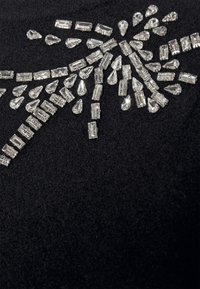 Czarna tkanina z rozsianym wzorem przezroczystych cyrkonii w różnych kształtach, w tym kropli i prostokątów, tworząc dynamiczny wzór.