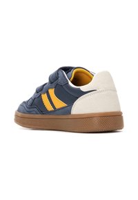 Zapatilla marine y amarilla con una cinta de velcro, que presenta una parte trasera texturizada en gris, suela de goma y únicas franjas horizontales naranjas.