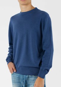 Niebieski dzianinowy sweter z prążkowanym okrągłym dekoltem, długimi rękawami i dopasowanym prążkowanym dołem. Materiał wydaje się miękki i gładki.