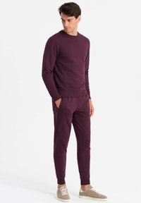 Bordeauxfarbener Sweatshirt mit Rundhalsausschnitt und gerippten Bündchen, kombiniert mit passenden schmal zulaufenden Hosen mit seitlichen Taschen und einem elastischen Bund.