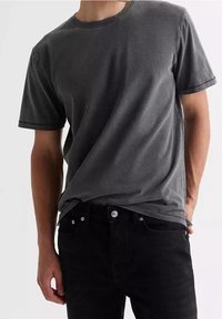T-shirt in cotone grigio con maniche corte e scollatura a girocollo. Tessuto morbido e vestibilità leggermente rilassata, indossata con jeans di denim neri.