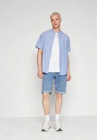 Helehall sinine lühikeste varrukatega nööbitav särk valge t-särgi peal, sellega sobitatud pööratud äärtega teksapüksid ja valged tossud. Sile kangas, vabaaja disain.