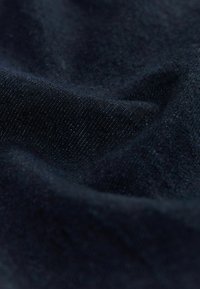 Donker marineblauwe stof met een zachte, textuurrijke oppervlakte. De weving is fijn en licht gemêleerd, waardoor het licht subtiel over de stof weerkaatst.