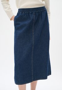 Denim midi kjol med elastisk midja, djupblå färg, sidofickor och synlig söm längs sömmarna.