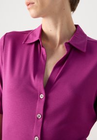 Fuchsia knoopshirt met een kraag en een gladde textuur, voorzien van kleine witte knopen en een klassieke pasvorm.