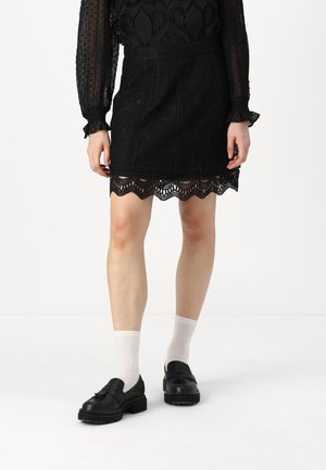 Black lace skirt with a scalloped hem, featuring intricate patterns and cut-outs. Worn with black shoes and white socks.