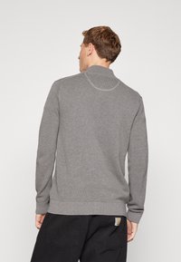 Suéter de punto gris con cuello alto, patrón texturizado y puños y dobladillo acanalados. Detalle de costura notable en la parte posterior.
