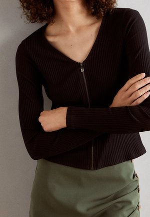 Czarna, żeberkowa bluzka z długim rękawem, wycięciem w serek i zapięciem na zamek, połączona z zieloną spódnicą o dopasowanym kroju z bocznymi guzikami i gładką teksturą.