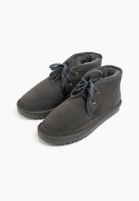 Stivaletti alla caviglia in suede grigio con una morbida fodera interna, dotati di lacci grigi e occhielli color oro, su una suola in gomma nera texturizzata.