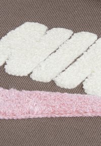 Taupe spalvos marškinėliai su minkštais, baltais raidžių siuviniais ir švelnia, tekstūruota rožine juostele. Medžiaga atrodo megzta su lygiu paviršiumi.