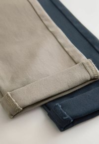 Két pár felhajtott szegélyű nadrág bézs és tengerészkék színekben. Mindkét nadrág sima textúrájú, és erősölt varrással rendelkezik a szegélyek mentén.