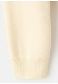 Gros plan d'un poignet de manche en maille côtelée beige sur un vêtement en tissu doux.