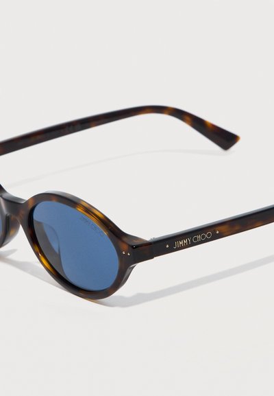 Οβάλ γυαλιά ηλίου σε χρώμα χελώνας με μπλε φακούς και το λογότυπο "JIMMY CHOO" σε χρυσό στο πλαϊνό μπράτσο.
