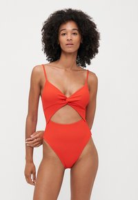 Maillot de bain une pièce rouge à côtes avec bretelles spaghetti, détail frontal tordu et côtés découpés, présentant un design à jambe haute.