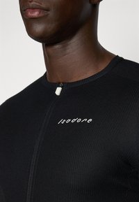 Svart zip-up plagg med ribbet tekstur. Har en hvit logo "Isadore" på brystet og en kontrastfarget glidelåshooker.