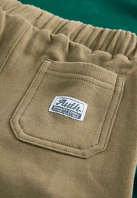 Pantalons kaki avec une taille élastique texturée et une poche arrière ornée d'une étiquette cousue. Le matériau est doux et légèrement extensible.