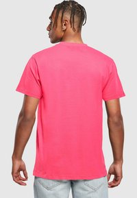 Rožinė medvilninė marškinė su trumpomis rankovėmis ir apvaliu kaklu. Audinys atrodo minkštas ir lygus, su paprastu dizainu ir be matomų raštų.