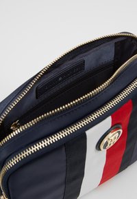 La bagage synthetique marine avec des rayures rouges, blanches et noires. Fermeture éclair et accessoires dorés, intérieur doublé avec une étiquette. Forme rectangulaire compacte.