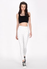 Zwart crop top met een vierkante halslijn, gecombineerd met wit geruite leggings en zwarte sneakers. De leggings hebben een gladde, rekbare stof.